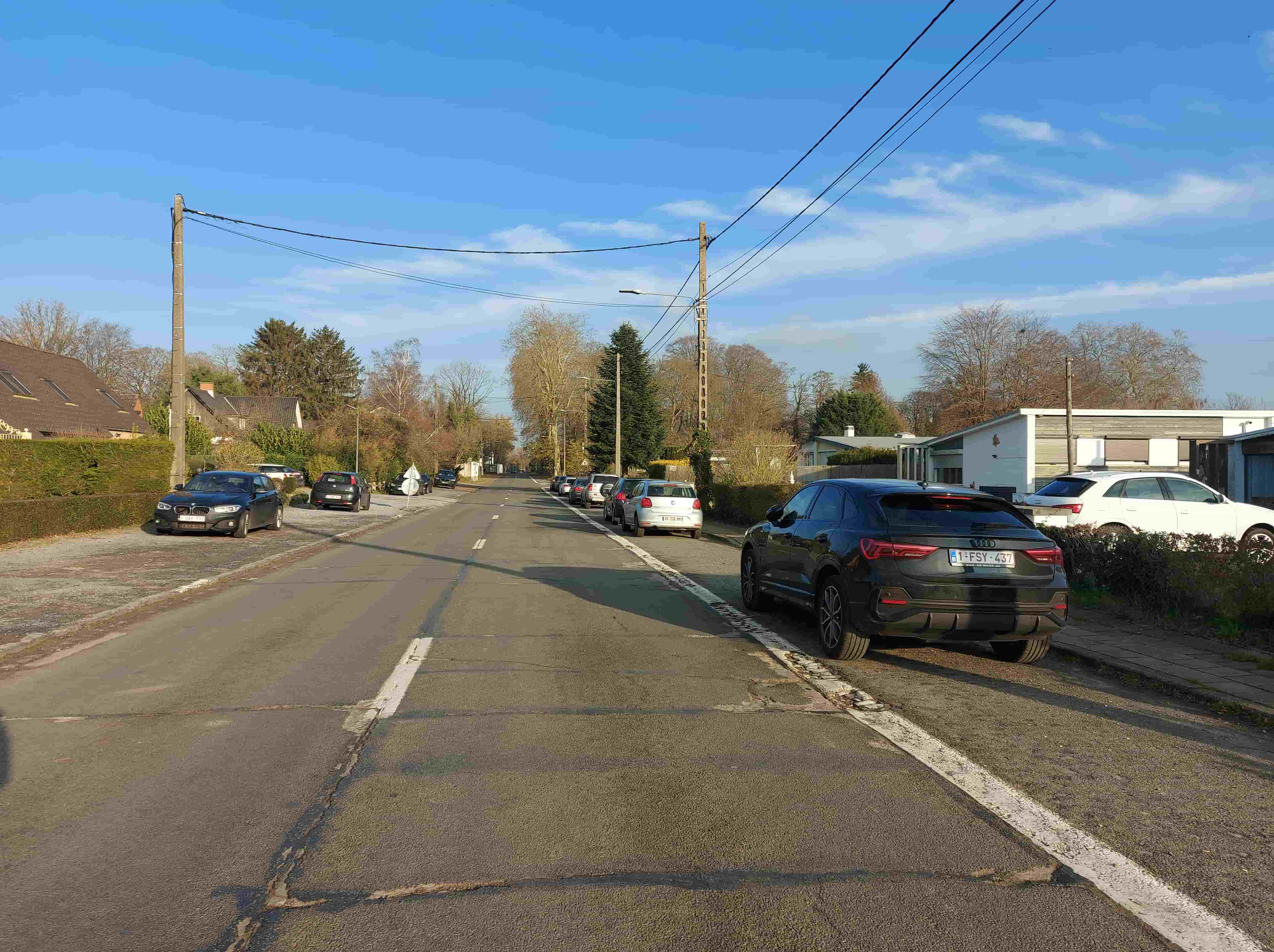 En tant qu'expert en code de la route belge, voici une analyse détaillée de l'image de la question d'examen :
Description Détaillée de la Situation Routière
L'image présente une vue en perspective le long d'une route droite, sous un ciel clair et ensoleillé, suggérant une journée lumineuse. La scène se déroule dans un environnement de type résidentiel ou de banlieue, caractérisé par la présence de maisons avec des toits en pente, de clôtures végétales (haies) et de nombreux arbres, certains dénudés de leurs feuilles, indiquant probablement l'hiver ou le début du printemps. Des poteaux électriques avec des câbles aériens longent la route des deux côtés.
Type de situation routière:
Il s'agit d'une section de route bidirectionnelle, probablement en agglomération ou sur une route publique de type local, compte tenu de la présence d'habitations et de véhicules stationnés. Ce n'est pas une intersection clairement visible au premier plan, mais la signalisation au loin (priorité de droite) indique qu'une intersection approche. La route est caractérisée par la présence d'accotements sur lesquels des véhicules sont stationnés.
Éléments visibles:
Véhicules:
À droite, au premier plan: Un SUV noir (Audi Q3, plaque belge 1-FSY-437), le véhicule en question, est stationné sur l'accotement, orienté dans le sens de la route (s'éloignant du photographe).
À droite, plus loin: Plusieurs autres véhicules sont stationnés en ligne sur le même accotement, dont un SUV blanc (également une Audi Q3) juste derrière le véhicule noir, puis d'autres voitures de diverses couleurs (claire, foncée).
À gauche, au premier plan: Une voiture noire (BMW série 1, plaque belge 1-JBY-713) est stationnée sur l'accotement, orientée face au photographe (dans le sens inverse de la marche du véhicule noir).
À gauche, plus loin: D'autres véhicules sont stationnés le long de l'accotement, notamment une Fiat Punto rouge et une Volkswagen Polo blanche, orientés dans différentes directions.
Il n'y a pas de véhicules en mouvement visibles sur la chaussée.
Panneaux de signalisation:
À gauche, au loin: Un panneau circulaire blanc à bord rouge et barre diagonale rouge (panneau C3) est visible, partiellement masqué par un véhicule et la végétation. Il indique une interdiction de stationnement.
À droite, au loin: Un panneau jaune en forme de losange à bord blanc et symbole noir (panneau B9) est visible. Il signale une priorité de droite à la prochaine intersection.
Il n'y a pas de panneau de stationnement réglementé (par exemple, panneau P avec indication de durée) visible à proximité immédiate du véhicule noir en panne.
Feux:
Des luminaires publics (lampadaires) sont visibles le long de la route, mais aucun feu de signalisation de trafic n'est présent.
Marquages au sol:
À droite: Une ligne blanche continue délimite clairement la chaussée (asphalte) de l'accotement pavé/en gravier sur lequel le véhicule noir est stationné. Cet accotement est manifestement de plain-pied avec la chaussée.
Au centre de la chaussée: Une ligne blanche discontinue est visible, indiquant une route à double sens de circulation où le dépassement est autorisé, ou le marquage central d'une voie.
À gauche: L'accotement est également présent, mais la délimitation par une ligne blanche continue n'est pas clairement visible sur toute la longueur, bien que le stationnement des véhicules s'y fasse.
Position et direction des véhicules:
Le véhicule noir (Audi Q3) visé par la question est stationné sur l'accotement droit, orienté dans le sens de la route (le pare-chocs arrière est face au photographe).
Les autres véhicules sur la droite sont également stationnés sur l'accotement droit, dans le même sens.
Le véhicule noir (BMW série 1) sur la gauche est stationné sur l'accotement gauche, orienté à contresens de la route par rapport au véhicule noir de droite (le pare-chocs avant est face au photographe).
Les autres véhicules sur la gauche sont stationnés sur l'accotement, certains dans un sens, d'autres dans l'autre.
Panneaux de signalisation présents et leur signification (reprise et précision):
Panneau C3 (à gauche, au loin): Indique une interdiction de stationnement à partir de ce point. Les véhicules peuvent s'y arrêter (arrêt temporaire pour embarquer/débarquer, etc.) mais ne peuvent pas y stationner (laisser le véhicule sans conducteur, ou avec conducteur mais pour une durée supérieure à celle nécessaire à un arrêt).
Panneau B9 (à droite, au loin): Indique que la priorité de droite s'applique à la prochaine intersection. Les conducteurs doivent céder le passage aux véhicules venant de leur droite.
Tout autre élément pertinent pour comprendre la situation:
Le contexte "en panne après un accident" est donné par la question. L'image seule ne montre pas de dégâts visibles sur le véhicule noir ni de signalisation d'urgence (phares de détresse, triangle de danger).
L'accotement sur lequel le véhicule noir est stationné est clairement un accotement de plain-pied, c'est-à-dire un accotement dont le niveau est le même que celui de la chaussée, délimité par une ligne continue. C'est un détail crucial pour la réglementation du stationnement en cas de panne.
• L'environnement est calme, peu de trafic ou d'activité humaine visible, ce qui est typique d'une zone résidentielle un jour ensoleillé.
Cette description fournit le cadre nécessaire pour répondre à la question spécifique concernant la durée maximale de stationnement du véhicule en panne sur l'accotement de plain-pied.