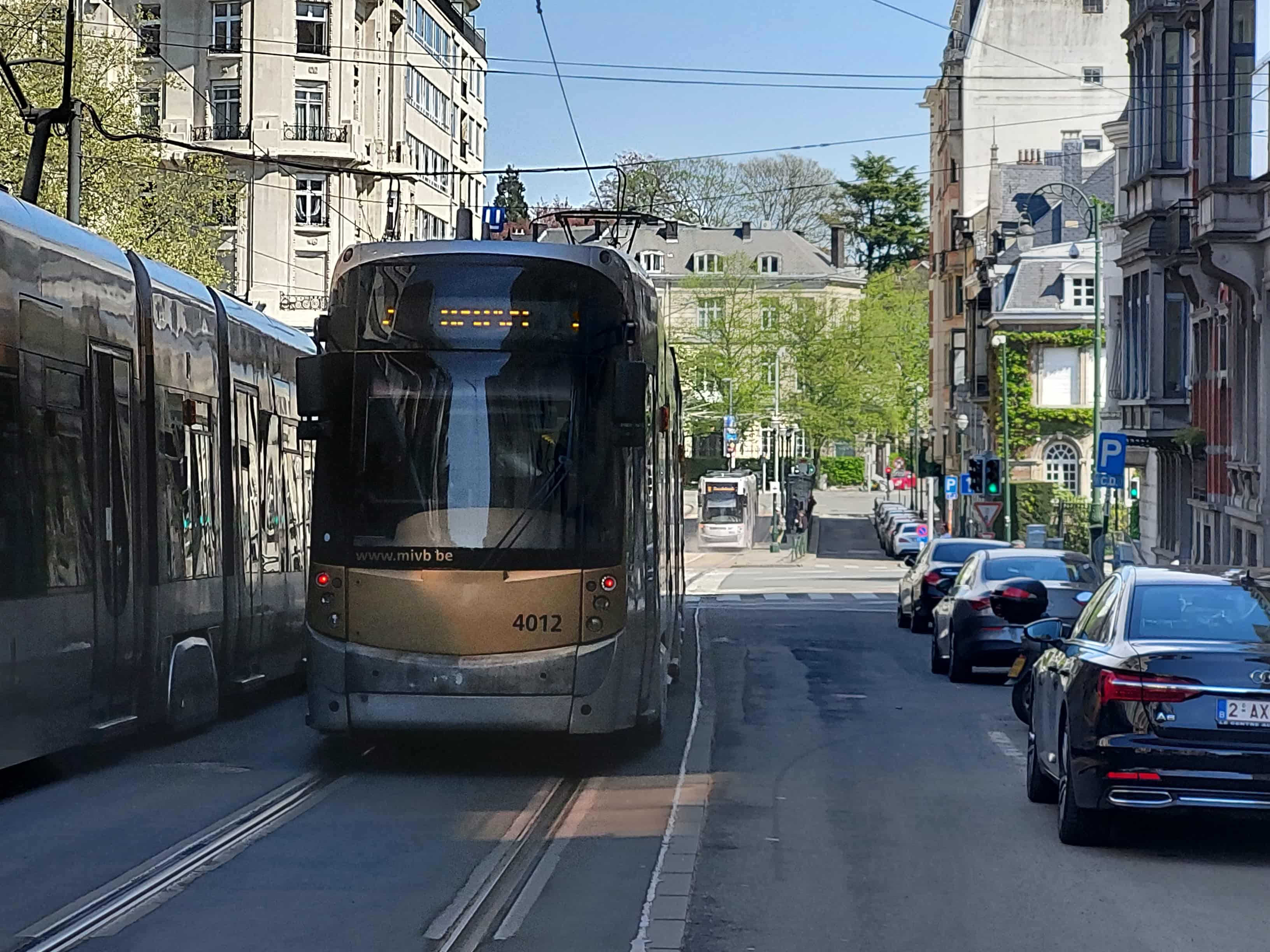 En tant qu'expert en code de la route belge, voici une description détaillée de la situation routière présentée dans l'image, conforme aux exigences pour une question d'examen de conduite :
Description Détaillée de la Situation Routière (Examen de Conduite Belge)
Contexte de la question: "Le tram est en mouvement, les véhicules à droite sont en stationnement."
Type de situation routière:
Il s'agit d'une rue urbaine, probablement à sens unique pour les véhicules motorisés ou à double sens mais avec les voies de tram au centre, située dans une zone bâtie dense (immeubles à plusieurs étages des deux côtés). La rue est caractérisée par la présence de voies de tramway. Plus loin, une intersection est visible, régulée par des feux de signalisation et où une autre rue (ou une bifurcation) s'embranche vers la droite.
Éléments visibles:
Véhicules:
Tram (au premier plan): Un tram moderne de la STIB/MIVB (numéro 4012), de couleur grise et beige, est positionné sur les voies de gauche, faisant face directement à l'observateur. Son pantographe est visible, connectant l'engin aux caténaires.
Tram (en arrière-plan): Un second tram, de couleur blanche, est visible plus loin dans la rue, également sur les voies de tram, semblant s'approcher ou être arrêté à l'intersection.
Voitures stationnées: Plusieurs voitures particulières sont garées en épi ou en bataille le long du trottoir droit. Au premier plan, une berline noire (Audi A5) est clairement visible, suivie de plusieurs autres véhicules (majoritairement blancs) alignés.
Panneaux de signalisation:
Panneau E9a (Panneau "P" bleu): Visible sur la droite, indiquant un emplacement où le stationnement est autorisé. En-dessous, une petite pancarte illisible mais typique des panneaux belges qui pourraient indiquer des conditions de stationnement (ex: "CD" pour carte de dérogation, "payant", "riverains").
Feu de signalisation tricolore (vert): Un feu pour véhicules est visible sur le côté droit de l'intersection lointaine, affichant une lumière verte. Un second feu tricolore est également visible plus loin à gauche.
Feu de signalisation pour tram (vertical blanc): Un feu spécifiquement destiné aux trams est visible juste au-dessus du tram au premier plan. Il affiche une barre verticale blanche, signifiant "autorisation de passer tout droit".
Panneau d'interdiction de stationner (E1, probable): Plus loin sur la droite, après le panneau "P", un panneau rond avec un contour rouge et une bande diagonale bleue est partiellement visible, suggérant un panneau d'interdiction de stationner (E1).
Marquages au sol:
Voies de tram: Deux ensembles de rails de tramway sont clairement visibles au centre-gauche de la chaussée, délimitant la zone de circulation des trams.
Ligne discontinue (potentielle): La chaussée semble suffisamment large pour permettre la circulation de véhicules à côté des voies de tram, mais aucune ligne de séparation de voie n'est clairement visible.
Bande blanche continue: Une ligne blanche continue délimite le bord de la chaussée où les voitures sont stationnées sur la droite.
Passage pour piétons (zébra): Juste devant le tram au premier plan, des bandes blanches sur la chaussée suggèrent la présence d'un passage pour piétons, bien que partiellement masqué par le tram.
Autres éléments:
Bâtiments: Des immeubles résidentiels ou commerciaux de style urbain bruxellois bordent la rue des deux côtés.
Poteaux et caténaires: De nombreux poteaux supportent les câbles électriques (caténaires) nécessaires à l'alimentation des trams, ainsi que l'éclairage public.
Trottoirs: Des trottoirs sont présents le long des bâtiments.
Végétation: Des arbres avec un feuillage printanier sont visibles, notamment à l'arrière-plan et le long des rues.
Position et direction des véhicules:
Tram (au premier plan): Se trouve sur les voies de tram les plus proches de l'observateur, faisant face à la caméra. Compte tenu du contexte "en mouvement" et du feu de tram vert, il est en train d'avancer dans la direction de l'observateur, ou s'apprête à le faire.
Tram (en arrière-plan): Se trouve également sur les voies de tram, mais plus loin, et semble s'éloigner de l'observateur ou être arrêté à l'intersection.
Voitures stationnées: Sont garées sur le côté droit de la chaussée, faisant face à l'intersection (donc s'éloignant de l'observateur).
Panneaux de signalisation présents et leur signification (synthèse):
Panneau E9a (P bleu): Indique une zone de stationnement autorisé.
Feu de signalisation pour tram (barre verticale blanche): Signifie que le tram est autorisé à passer tout droit.
Feu de signalisation tricolore (vert): Indique que le passage est autorisé pour les véhicules dans la direction désignée.
Panneau E1 (rond rouge barré de bleu): (Probable au loin) Signifie "interdiction de stationner".
Tout autre élément pertinent pour comprendre la situation:
La scène dépeint une situation urbaine typique de Bruxelles, où les trams partagent l'espace routier avec d'autres véhicules et les piétons. La coexistence des voies de tram et des zones de stationnement sur une chaussée relativement étroite exige une vigilance particulière. Le fait que le tram soit en mouvement (confirmé par le contexte et le feu tram) indique une priorité potentielle ou une nécessité de manœuvre, tandis que les véhicules stationnés peuvent réduire la visibilité et créer des situations imprévues (ouverture de portières, piétons émergeant entre les véhicules). La présence d'un passage pour piétons (probable) ajoute une couche de complexité, nécessitant d'être attentif aux usagers faibles.
