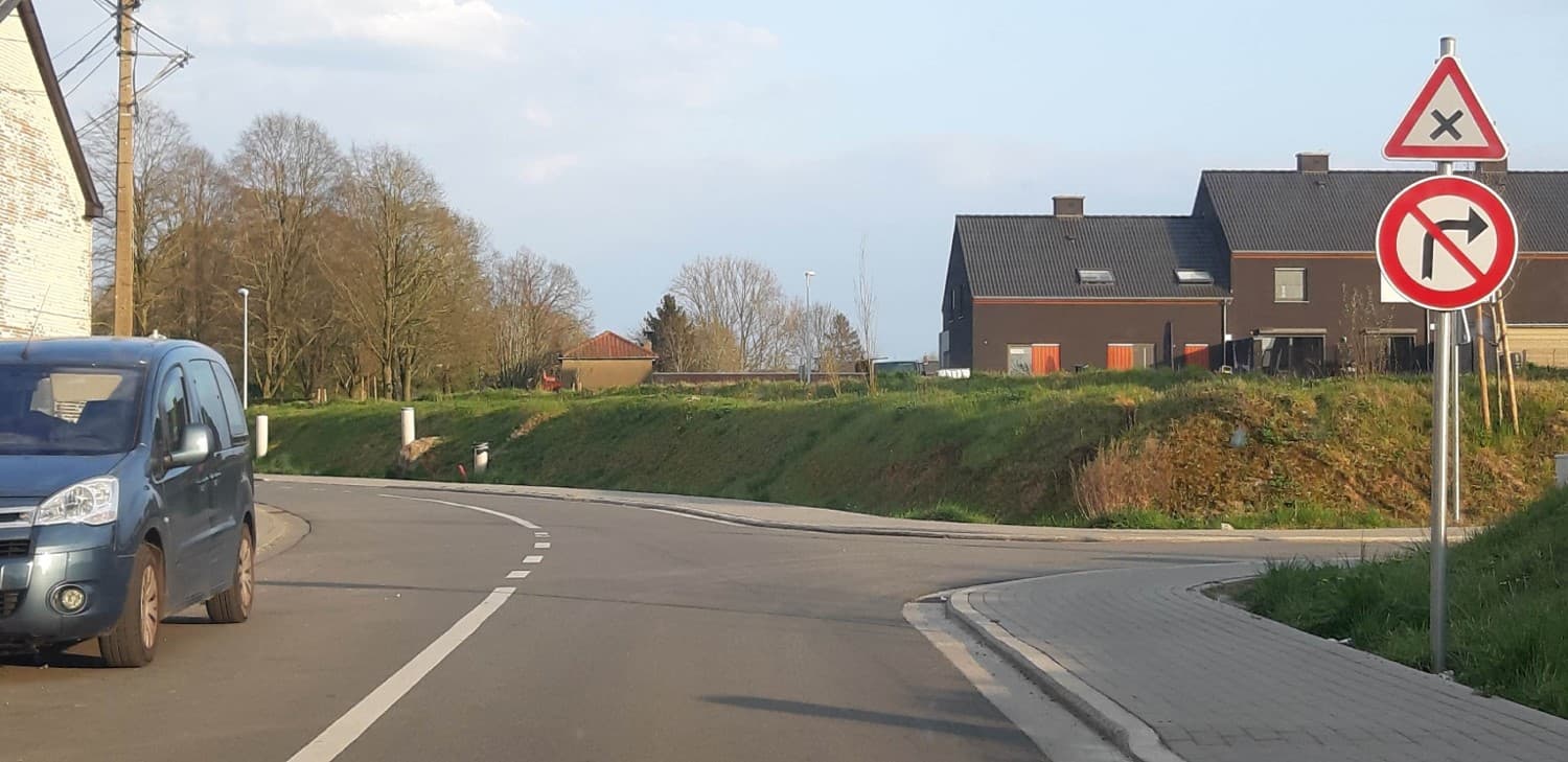 En tant qu'expert en code de la route belge, voici une analyse détaillée de l'image pour comprendre le contexte de la question sur la priorité de droite :
Description détaillée de la situation routière :
Type de situation routière :
Nous sommes en présence d'une intersection en "T" ou d'un embranchement. Le véhicule d'où l'image est prise (le "véhicule caméra") approche de cette intersection sur une route qui semble être la voie principale, légèrement incurvée vers la droite. Sur la droite de cette route principale, une autre voie débouche, formant l'intersection. Le contexte général est une zone semi-urbaine ou rurale, avec des habitations et de la végétation.
Éléments visibles :
Véhicules : Un véhicule de type monospace (ressemblant à un Citroën Berlingo ou similaire) de couleur bleu-gris est visible sur le côté gauche de la route principale, partiellement masqué par le bord gauche de l'image. Son avant est orienté vers l'avant, le long de la route principale. Il semble être garé ou à l'arrêt, ou en train de circuler dans la direction opposée à celle du véhicule caméra.
Panneaux de signalisation : Deux panneaux sont superposés sur un même poteau, positionné à droite de la chaussée, juste avant l'intersection :
Panneau supérieur (A21) : C'est un panneau de danger triangulaire à fond blanc, bordé de rouge, avec une croix de Saint-André noire en son centre. En Belgique, ce panneau indique une "Intersection où la priorité de droite est applicable". Cela signifie que tous les conducteurs qui se présentent à cette intersection doivent céder le passage aux conducteurs venant de leur droite, à moins qu'une autre signalisation ne déroge à cette règle pour une voie spécifique.
Panneau inférieur (C3a) : C'est un panneau d'interdiction circulaire à fond blanc, bordé de rouge, avec une flèche noire pointant vers la droite et barrée d'une bande diagonale rouge. En Belgique, ce panneau signifie "Interdiction de tourner à droite".
Feux : Aucun feu de signalisation n'est visible.
Marquages au sol :
Une ligne blanche continue délimite le bord gauche de la chaussée du véhicule caméra.
Une ligne discontinue blanche sépare ce qui pourrait être deux voies de circulation ou indique le centre de la chaussée si elle est à double sens. Cette ligne suit la courbure de la route.
Aucun marquage spécifique de priorité (triangle "cédez le passage" ou ligne d'arrêt) n'est visible pour la route d'où provient le véhicule caméra.
Aménagements routiers et environnement :
Une voie piétonne ou un trottoir pavé est visible sur le côté droit de l'image, longeant l'intersection.
De l'herbe et des talus verdoyants bordent les routes.
Des arbres dénudés (suggérant l'hiver ou le début du printemps) et des bâtiments (une maison en briques claires à gauche, des maisons modernes sombres à droite, derrière les panneaux) sont visibles en arrière-plan.
Des poteaux d'éclairage public et un poteau électrique sont également présents.
Position et direction des véhicules :
Le véhicule caméra est en approche de l'intersection, suivant la courbure de la route principale.
Le monospace bleu-gris est positionné sur le côté gauche de la chaussée du véhicule caméra, faisant face dans la direction de l'approche du véhicule caméra (ou très légèrement décalé). Il ne semble pas être en mouvement dans l'immédiat.
Panneaux de signalisation présents et leur signification :
Panneau A21 ("Croix de Saint-André") : Il avertit que l'intersection qui va suivre est une intersection où la règle générale de la priorité de droite est d'application. Chaque conducteur arrivant à cette intersection doit laisser la priorité aux véhicules qui viennent de sa droite.
Panneau C3a ("Interdiction de tourner à droite") : Il informe le conducteur du véhicule caméra qu'il lui est interdit de s'engager dans la voie débouchant à droite à cette intersection.
Tout autre élément pertinent pour comprendre la situation :
L'emplacement des panneaux est crucial. Ils s'adressent clairement au conducteur du véhicule caméra. Le panneau A21 indique que la priorité de droite s'applique à toute l'intersection. Le panneau C3a, situé en dessous, vient ajouter une contrainte spécifique : le conducteur ne peut pas tourner à droite.
En résumé pour la question "Cette priorité de droite signifie :", cela signifie que :
Même si le conducteur ne peut pas tourner à droite, s'il continue tout droit ou tourne à gauche, il devrait théoriquement céder le passage à tout véhicule qui viendrait de la voie de droite (bien que celle-ci nous soit interdite d'accès).
De même, si un véhicule (comme le monospace bleu-gris si il était en mouvement et venait d'une voie "à notre gauche") approchait de l'intersection et voulait tourner, il devrait nous céder la priorité si nous nous trouvions à sa droite, selon la règle générale.
La question vise à tester la compréhension que le panneau A21 établit la règle de la priorité de droite pour l'ensemble de l'intersection, indépendamment des autres manœuvres autorisées ou interdites. Le fait qu'il soit interdit de tourner à droite ne dispense pas de la règle de priorité de droite pour les autres flux de circulation (par exemple, si nous allions tout droit et qu'un véhicule arrivait de la droite – ce qui est peu probable ici, mais l'idée est que la règle est générale pour l'intersection). En l'absence de toute autre signalisation spécifique pour la route principale, le conducteur du véhicule caméra est soumis à la priorité de droite vis-à-vis des usagers venant de sa droite et a priorité sur ceux venant de sa gauche.