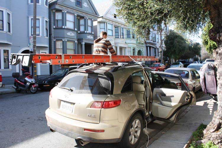 En tant qu'expert en code de la route belge, voici une description détaillée de la situation présente dans l'image, en tenant compte du contexte de la question posée :
Description Détaillée de la Situation Routière pour un Examen de Conduite Belge
L'image présente une scène de rue urbaine ou résidentielle en plein jour, sous un ciel ensoleillé.
Type de situation routière :
Il s'agit d'une rue bordée de trottoirs et de maisons mitoyennes, typique d'un environnement urbain ou de faubourg. Le véhicule principal est stationné (ou à l'arrêt pour une opération de chargement/déchargement) le long du trottoir, sur le côté droit de la chaussée (du point de vue du véhicule). Il n'y a pas d'intersection, de carrefour giratoire ou de zone particulière visible, mais plutôt un segment de rue.
Éléments visibles :
Véhicules :
Véhicule principal : Au premier plan, un SUV de couleur beige clair (identifié comme un Infiniti FX35 grâce à son insigne arrière) est stationné. Il est équipé d'une galerie de toit sur laquelle est fixée une longue échelle de couleur orange et blanche. Les portes arrière droite et avant droite du SUV sont ouvertes, suggérant que le véhicule est en cours de préparation ou d'une opération.
Charge : L'échelle, clairement visible, dépasse considérablement de l'arrière du SUV. Le contexte de la question précise un dépassement de 1,1 mètre.
Autres véhicules : Un scooter rouge et noir est garé sur le trottoir ou juste en bordure de celui-ci, à l'avant gauche du SUV. Plusieurs autres voitures sont stationnées le long du trottoir, à l'avant du SUV (une voiture foncée est visible) et plus loin dans la rue.
Environnement :
Bâtiments : Une rangée de maisons de ville de plusieurs étages, avec une architecture distinctive (possiblement victorienne ou édouardienne, suggérant un contexte non-belge, mais l'analyse se fait selon le code belge pour la question).
Végétation : Un grand arbre avec un tronc rugueux et un feuillage dense est visible sur le trottoir, à droite du SUV, masquant partiellement la vue vers l'avant de la rue. D'autres arbres sont visibles plus loin.
Infrastructure routière : La chaussée est asphaltée. Un trottoir de largeur respectable borde la chaussée. Un poteau utilitaire (avec des petites plaques qui ne sont pas des panneaux du code de la route belge) est visible à l'avant gauche de l'échelle.
• Personnes : Une personne est assise ou accroupie sur le toit du SUV, au niveau de la galerie de toit, visiblement en train de manipuler l'échelle ou de sécuriser son chargement.
Position et direction des véhicules :
Le SUV beige est garé parallèlement au trottoir, orienté vers l'avant de la rue (vers le fond de l'image). Les autres véhicules stationnés sont également dans la même direction générale. Le scooter est garé face à la même direction générale, légèrement en avant du SUV.
Panneaux de signalisation présents et leur signification :
Il n'y a aucun panneau de signalisation routière conforme au code de la route belge clairement identifiable sur l'image. Le poteau utilitaire visible porte de petites plaques qui semblent être des régulations de stationnement locales (probablement américaines, étant donné l'immatriculation du véhicule), mais elles ne sont pas des panneaux de signalisation routière belges. L'absence de signalisation spécifique belge est une observation importante pour l'expert.
Tout autre élément pertinent pour comprendre la situation :
L'élément le plus pertinent pour la question est le chargement de l'échelle sur la galerie de toit du SUV, et son dépassement significatif à l'arrière du véhicule. La présence d'une personne manipulant l'échelle et les portes ouvertes indiquent une opération en cours liée au chargement. La question se concentre spécifiquement sur l'obligation de signaler ce dépassement de 1,1 mètre selon la réglementation belge.