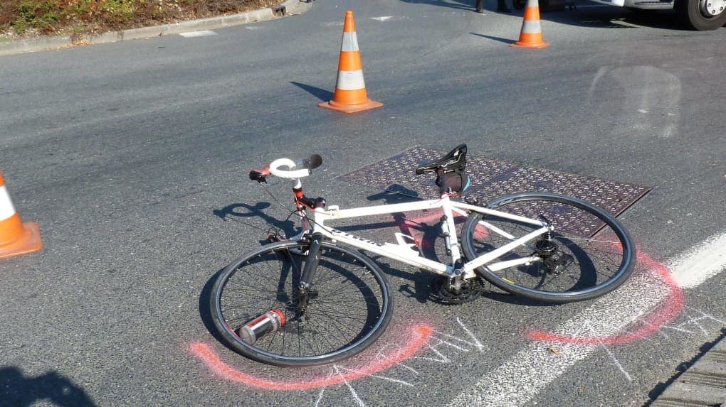 En tant qu'expert en code de la route belge, voici une description détaillée de l'image pour comprendre le contexte de la question :
Contexte de la question: "Vous venez de renverser un cycliste. Que faîtes-vous en premier ?"
Description détaillée de la situation routière:
L'image présente une scène de rue, en plein jour et sous une lumière vive (ombres prononcées), qui semble être l'après-coup d'un accident de la circulation impliquant un cycliste.
Type de situation routière:
Il s'agit d'une section de route asphaltée, probablement en milieu urbain ou périurbain, à en juger par la présence d'une bordure de trottoir sur le côté gauche de l'image et d'une plaque d'égout sur la chaussée. Il ne s'agit pas clairement d'une intersection majeure, mais pourrait être à proximité d'un carrefour, d'un accès ou d'un passage. La présence de marquages au sol suggère une zone où la signalisation est habituellement présente.
Éléments visibles:
Véhicules:
Un vélo de route (vélo de course) de couleur blanche est couché sur le flanc droit au milieu de la chaussée. Il est l'élément central de l'image. Un bidon d'eau est visible sur le porte-bidon fixé au cadre, tombé près de la roue avant.
Une partie d'un véhicule plus grand (semblant être un utilitaire, une camionnette ou un camion léger, visible par sa roue avant droite et une partie de sa carrosserie blanche) est visible dans le coin supérieur droit de l'image. Il semble être stationné ou à l'arrêt, légèrement en retrait et orienté dans le sens de la route.
Panneaux de signalisation: Aucun panneau de signalisation routière permanent n'est visible dans l'image.
Feux de circulation: Aucun feu de circulation n'est visible.
Marquages au sol:
Une épaisse ligne blanche continue est visible sur le côté droit de la chaussée, délimitant potentiellement le bord de la route, un emplacement de stationnement, ou une bande cyclable/piétonne.
Des marquages en spray de couleur rouge sont clairement visibles sur l'asphalte, encerclant partiellement la roue avant du vélo et formant des arcs et des traits, typiques des relevés d'accident effectués par les services d'urgence ou la police pour documenter la position des véhicules et des indices.
Des marquages à la craie ou à la peinture blanche sont également visibles, notamment des traits et des chiffres discrets près des marquages rouges, confirmant l'étape de documentation post-accident.
Autres éléments:
Trois cônes de signalisation (plots orange et blancs) sont disposés sur la chaussée. Un est au premier plan à gauche, un autre plus loin au centre de l'image, et un troisième est partiellement visible derrière le véhicule en haut à droite. Ces cônes servent à signaler un danger et à sécuriser la zone de l'accident.
Une plaque d'égout métallique est incrustée dans l'asphalte, juste derrière la roue arrière du vélo.
Une bordure de trottoir est visible sur le côté gauche de la route, avec de la végétation basse derrière elle.
Position et direction des véhicules:
Le vélo est couché, globalement orienté en diagonale par rapport à l'axe de la route, avec sa roue avant pointant vers le bas-gauche de l'image et sa roue arrière vers le haut-droit. Il repose sur la chaussée, par-dessus la plaque d'égout.
Le véhicule plus grand est visible partiellement en haut à droite. Il semble être positionné parallèlement à l'axe de la route, stationné ou arrêté sur le côté, à une certaine distance du vélo. Sa direction précise n'est pas clairement discernable, mais il n'apparaît pas en mouvement.
Panneaux de signalisation présents et leur signification:
Comme mentionné, aucun panneau routier réglementaire n'est visible.
Les cônes de signalisation agissent comme des dispositifs de signalisation temporaires. Leur signification est "danger" ou "zone d'intervention / accident", invitant les autres usagers à la prudence et à contourner la zone balisée.
Tout autre élément pertinent pour comprendre la situation:
L'ensemble de la scène, avec le vélo au sol, les cônes de signalisation, et surtout les marquages au sol rouges et blancs, indique clairement que l'image a été prise après l'accident et que des mesures de sécurisation et de documentation par les services compétents (police, secours) ont déjà été mises en œuvre.
Il n'y a aucun blessé visible sur l'image, ni d'autres témoins actifs, ce qui renforce l'idée qu'il s'agit d'une photo d'investigation ou de constat.
• La question "Vous venez de renverser un cycliste. Que faîtes-vous en premier ?" est donc posée dans un contexte qui précède la scène photographiée. L'image montre les conséquences d'un non-respect des premières mesures à prendre après un accident, ou du moins, le résultat d'un accident qui a été pris en charge.